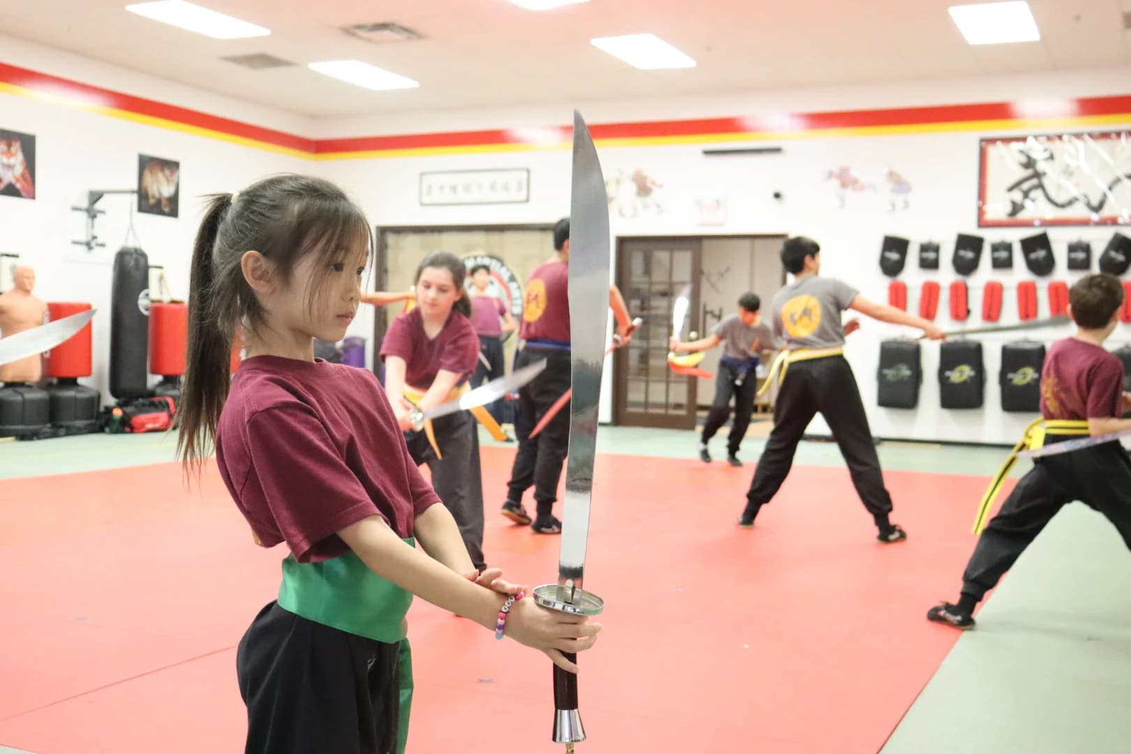 A girl holding a straight sword while classmates kick behind her